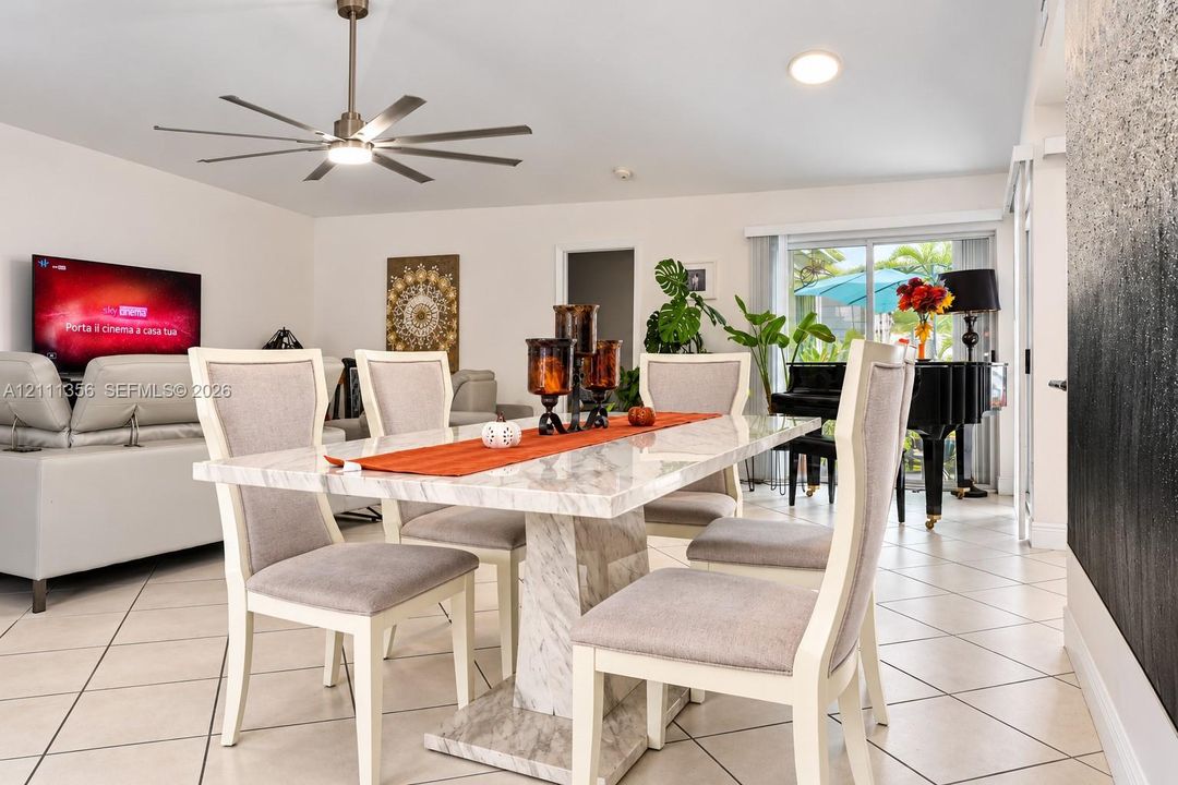 Open-concept interior featuring light-toned diagonal tile flooring, a multi-blade ceiling fan with integrated lighting, and glass sliding doors