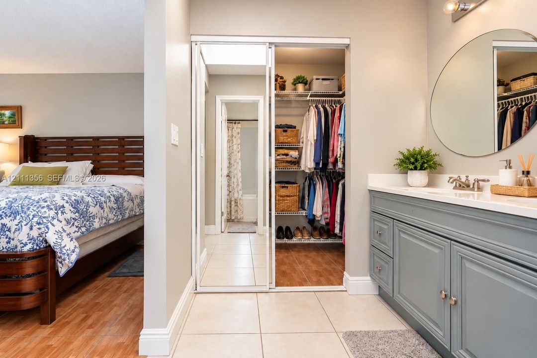 Vanity featuring a painted cabinet, solid surface countertop, and oval wall-mounted mirror, complemented by a reach-in closet with sliding mirrored doors and integrated wire shelving