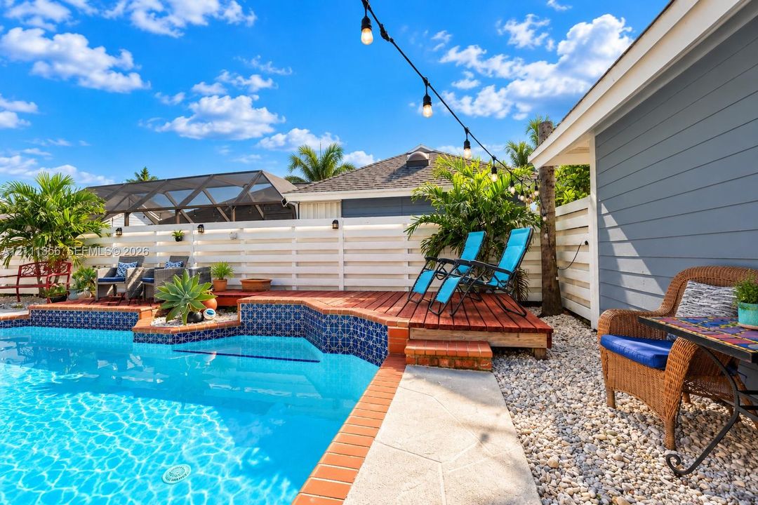 In-ground swimming pool with patterned tile border, raised wood decking, horizontal slat fencing, and stone landscape ground cover