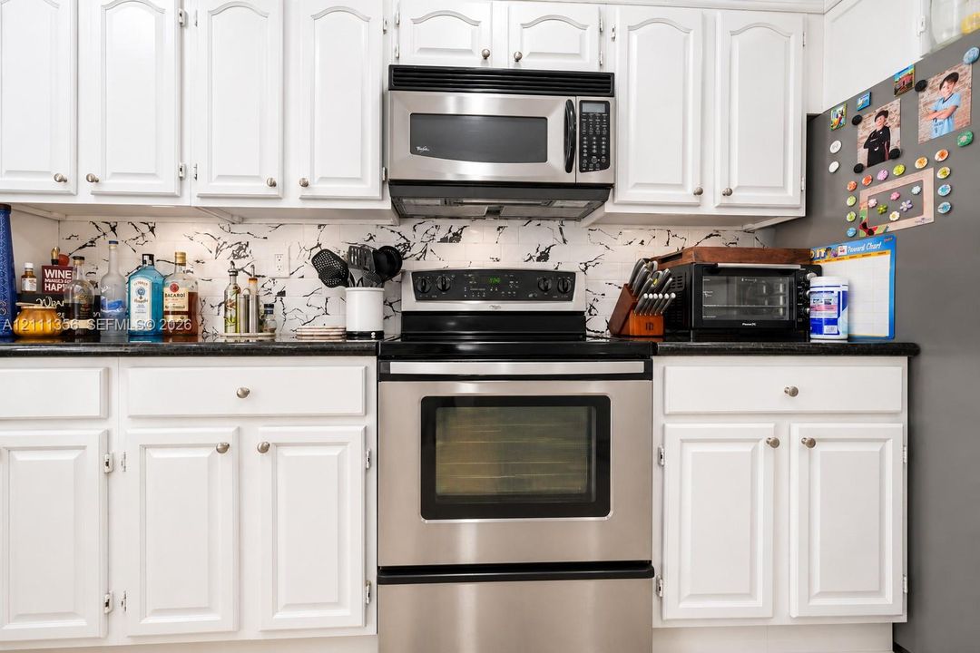 Kitchen featuring white raised-panel cabinetry, dark solid-surface countertops, patterned tile backsplash, and stainless steel appliances including an over-the-range microwave and range