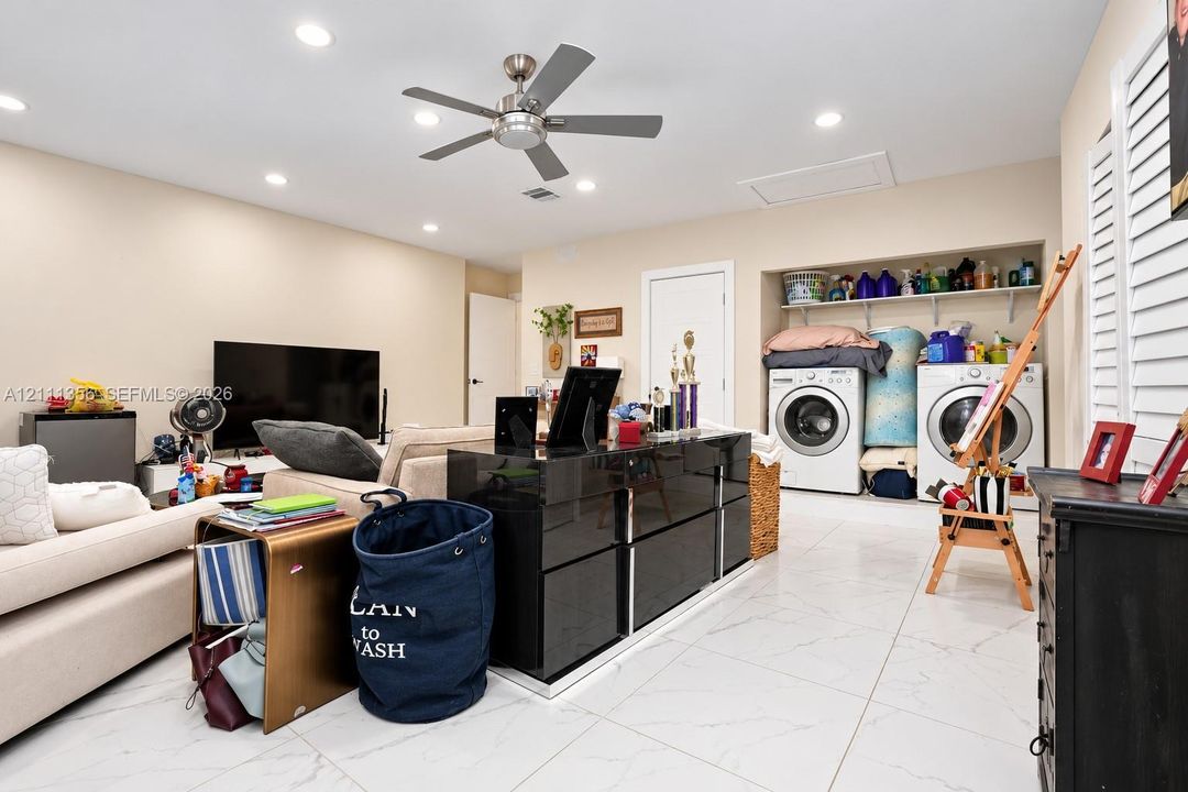 Large-format white tile flooring, recessed ceiling lighting, brushed metal ceiling fan, and built-in laundry area with overhead shelving
