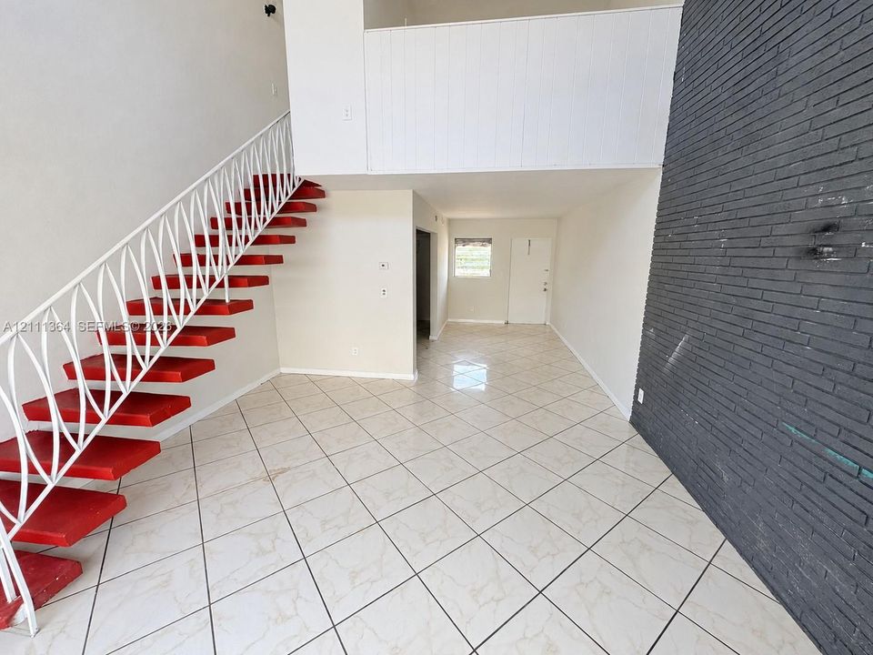 Open floor plan featuring high ceilings, a floor-to-ceiling dark brick accent wall, tile flooring in a diamond pattern, and a staircase with open risers and metal latticework railing