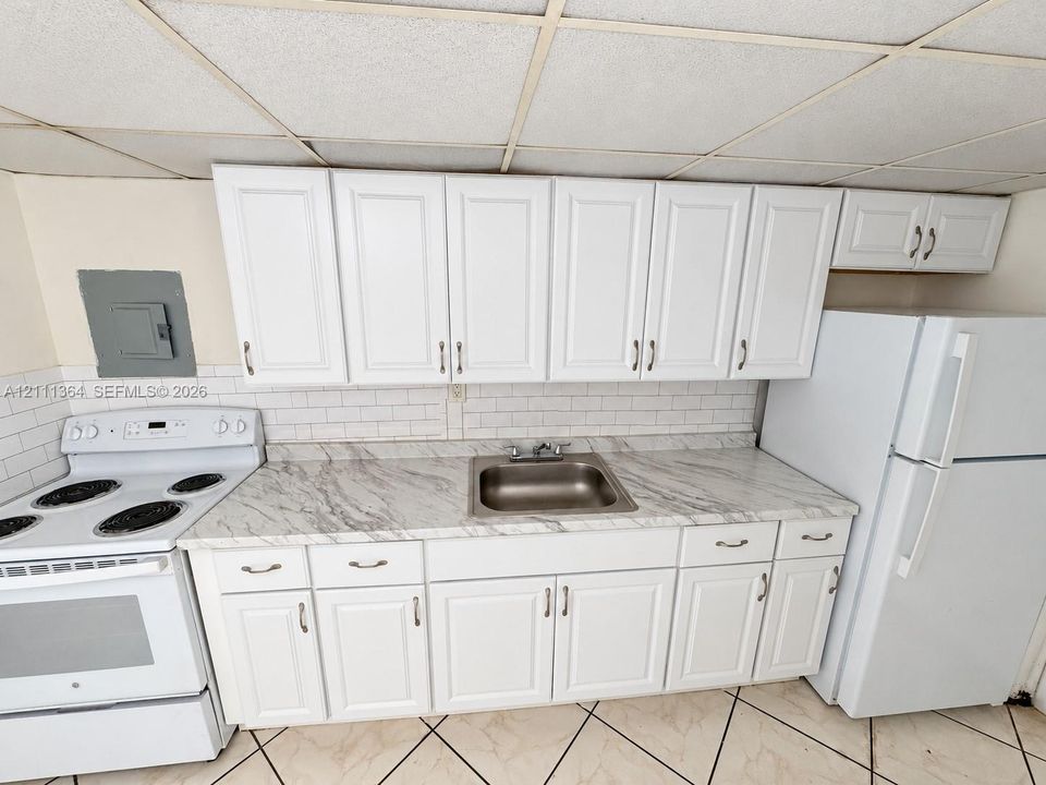 Kitchen featuring white shaker-style cabinetry, stone-patterned laminate countertops, white subway tile backsplash, stainless steel sink, and ceramic tile flooring