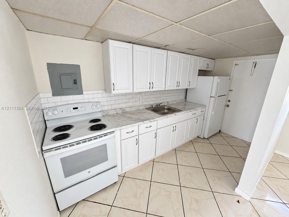 Kitchen featuring white shaker-style cabinetry, white subway tile backsplash, stone-finish countertops, stainless steel sink, and diamond-pattern tile flooring