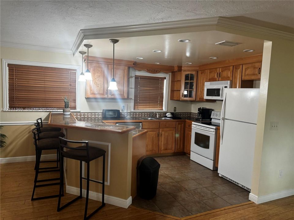 Kitchen featuring natural wood cabinetry, tiled backsplash, built-in microwave, wood-finish flooring, and a peninsula with a raised counter