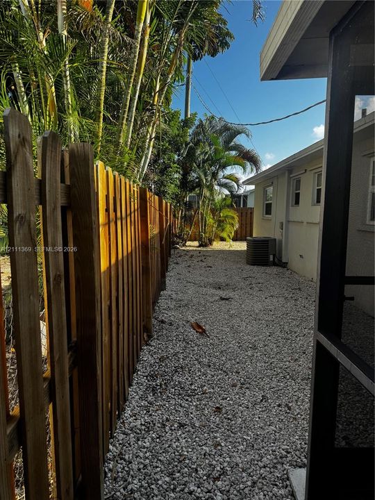 Side yard featuring vertical wood fencing, light-colored stone ground cover, and mature palm trees