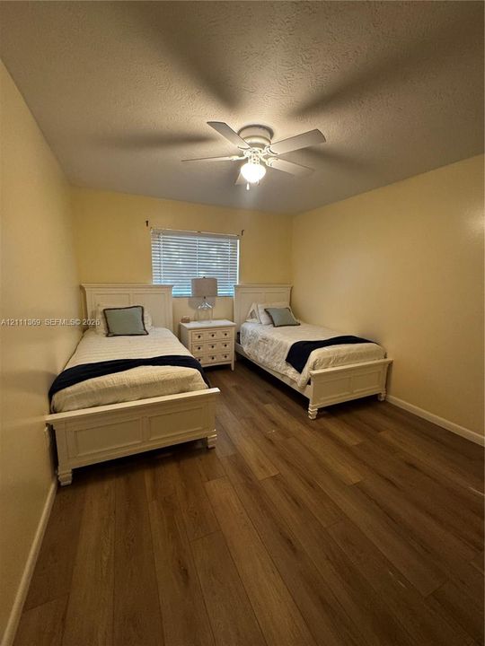 Bedroom featuring wood-finish flooring, a white ceiling fan with integrated light fixture, and horizontal blind window covering