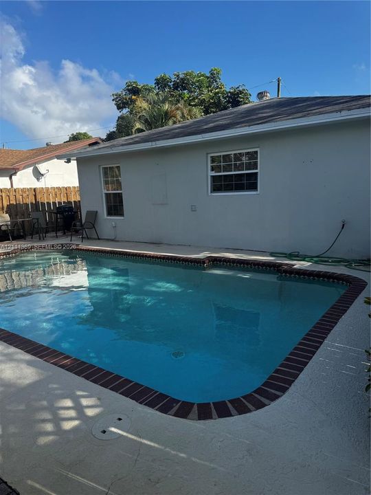 Swimming pool with brick-accented coping and concrete patio surround, featuring an enclosed backyard with wood-style fencing