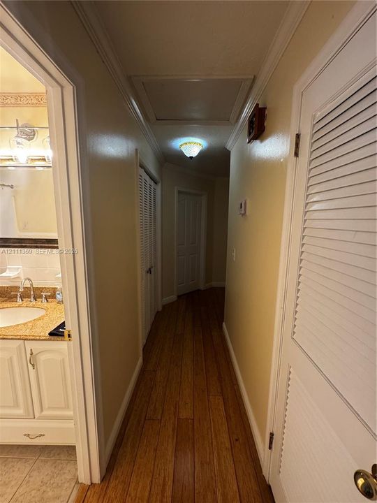 Hallway featuring wood-finish flooring, white louvered closet doors, and a ceiling-mounted light fixture