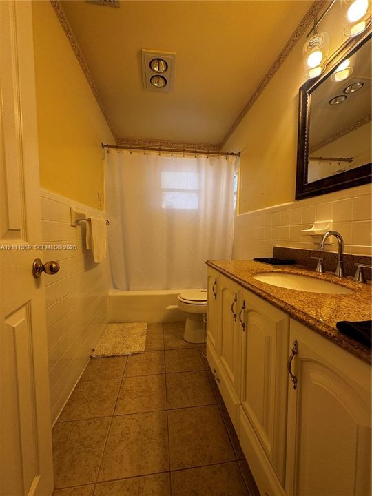 Bathroom featuring tile flooring, subway-style wall tiling, a vanity with a stone-finish countertop, an oval undermount sink, and a framed mirror