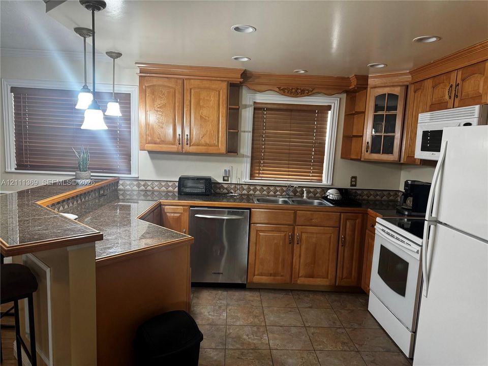 Kitchen featuring wooden cabinetry, laminate countertops with a breakfast bar, stainless steel dishwasher, tile flooring, and recessed lighting