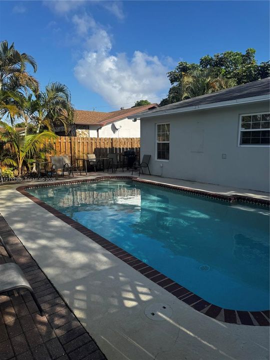 In-ground swimming pool with a brick-trimmed border, concrete patio, and wood privacy fencing