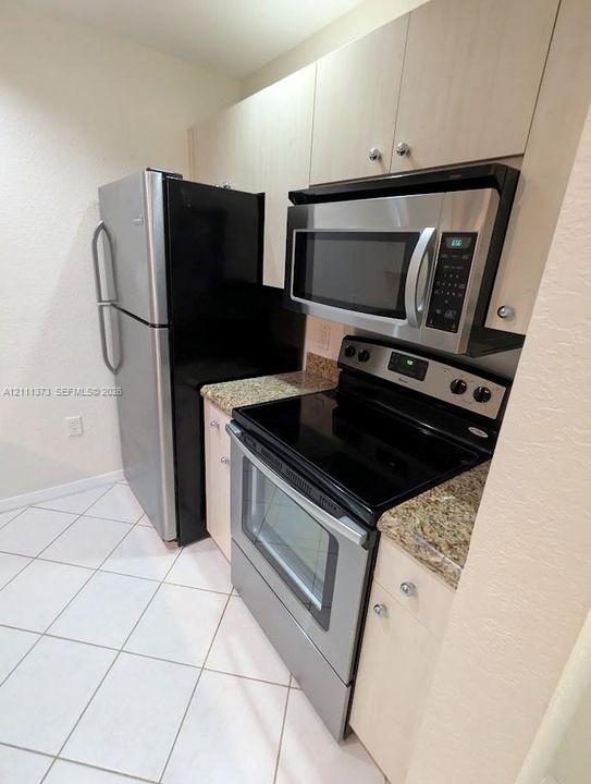 Kitchen featuring light-finish cabinetry, stone-style countertops, stainless steel appliances, and ceramic tile flooring