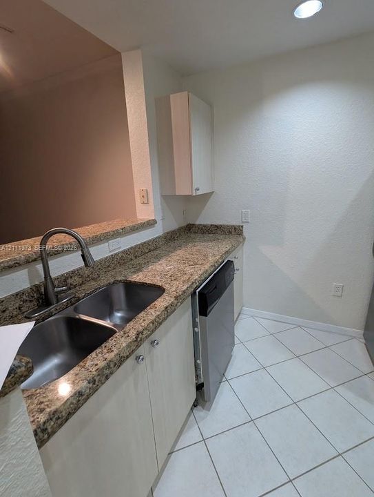 Kitchen featuring stone-finish countertops, stainless steel double-basin undermount sink with a gooseneck faucet, built-in dishwasher, light-finish cabinetry, and tiled flooring