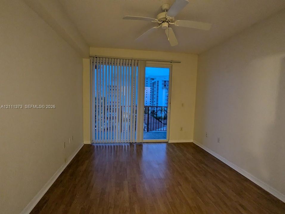 Interior space featuring wood-finish flooring, a ceiling fan with integrated light fixture, and floor-to-ceiling glass sliding doors opening to a balcony