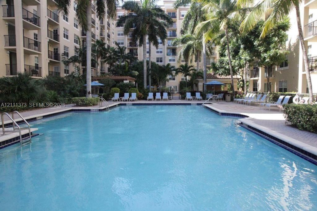 In-ground pool with paved surround, mature palm trees, and multi-story building exterior
