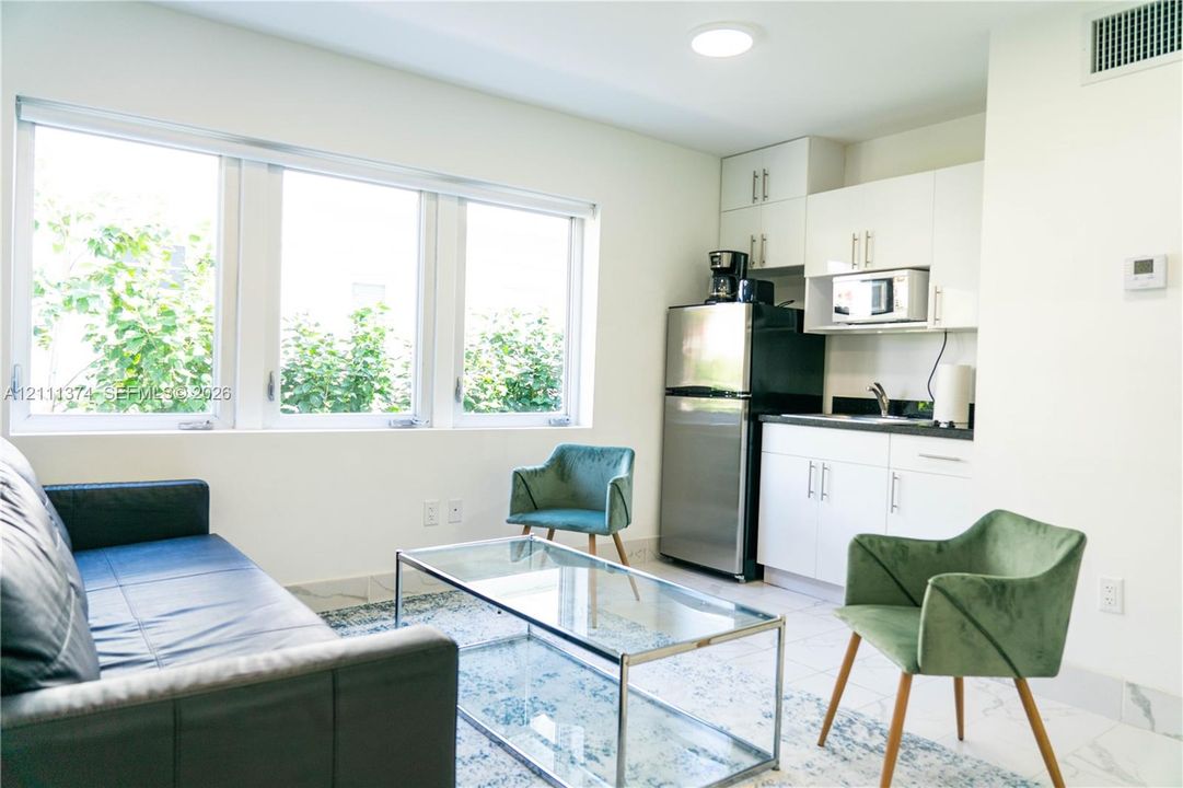 Kitchenette featuring white cabinetry, dark stone-finish countertops, stainless steel appliances, and large windows with natural lighting, complemented by tile flooring