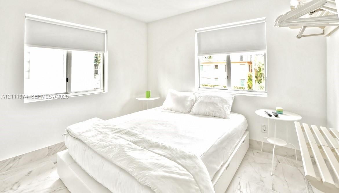 Bright room featuring white walls, stone-finish flooring, two large windows, and installed roller shades