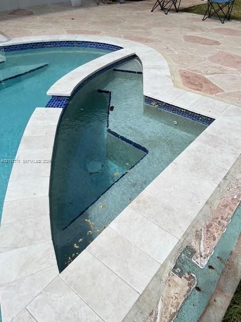 In-ground pool featuring an integrated spa with blue tile accents and light-toned stone coping, set within a flagstone patio