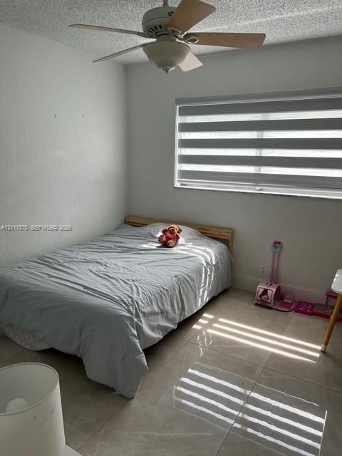 Neutral-toned tile flooring, ceiling fan with light fixture, and horizontal dual-layer window treatments