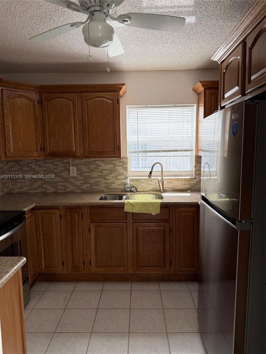 Kitchen featuring wood cabinetry, stone-finish countertops, tile backsplash, stainless steel sink with high-arc faucet, and tiled flooring