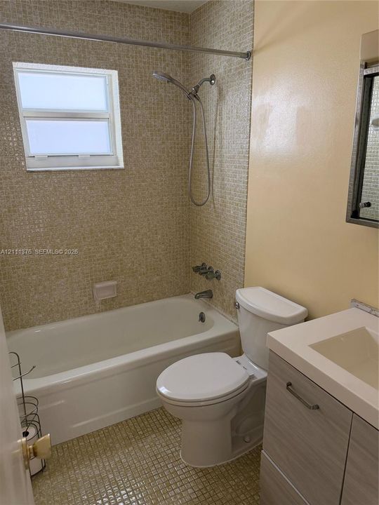 Bathroom featuring mosaic tile wall accents, a built-in bathtub with shower head, a wood-finish vanity with an integrated basin, and an inset window