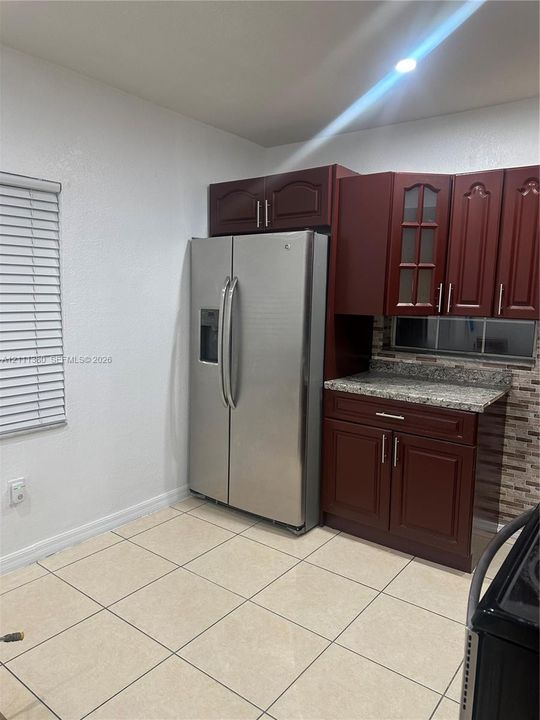 Kitchen area featuring raised-panel wood cabinetry, stone countertops, stainless steel side-by-side refrigerator, decorative tile backsplash, and tile flooring