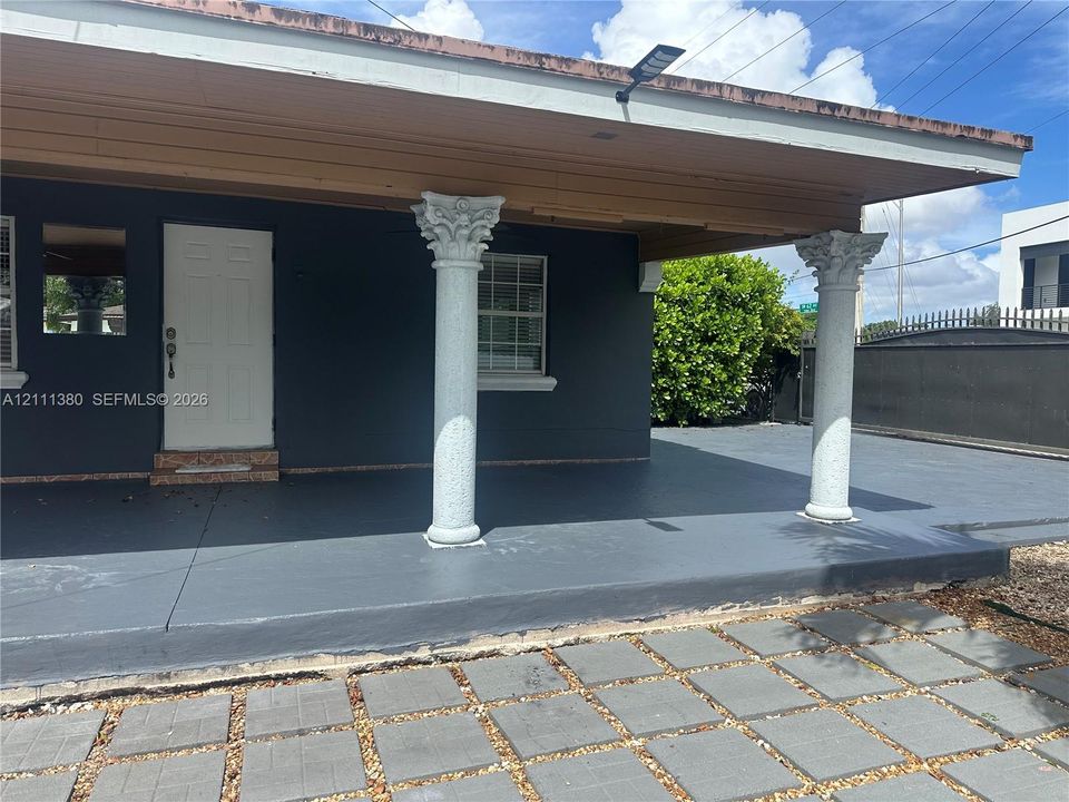 Covered front porch featuring decorative columns with ornate capitals, a paved hardscape entry, and a solid exterior door