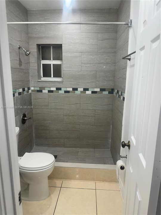 Walk-in shower featuring gray rectangular wall tile, a decorative mosaic tile accent border, a built-in window, and a wall-mounted shower head