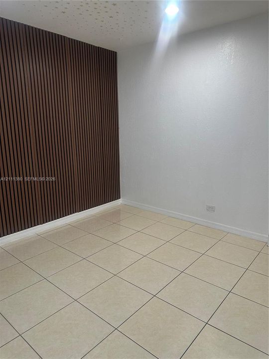 Interior space featuring vertical wood-slat accent wall, neutral large-format tile flooring, and integrated ceiling lighting