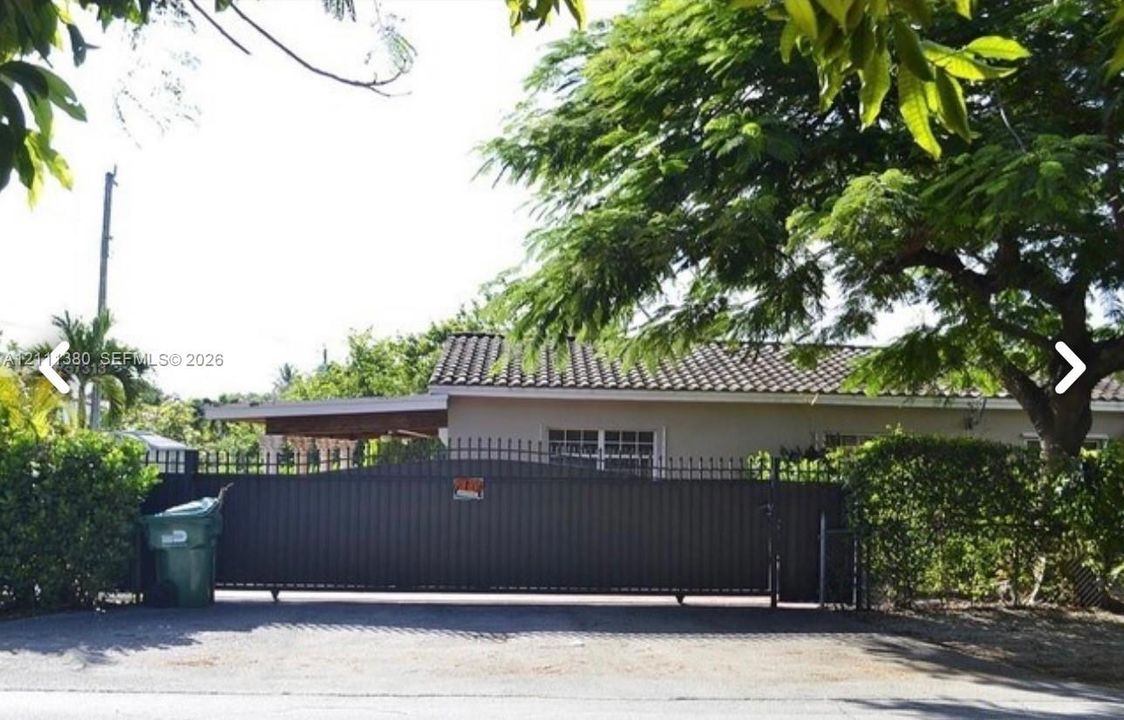 Gated property entrance featuring a full-width metal privacy gate, tile roof, and mature perimeter landscaping