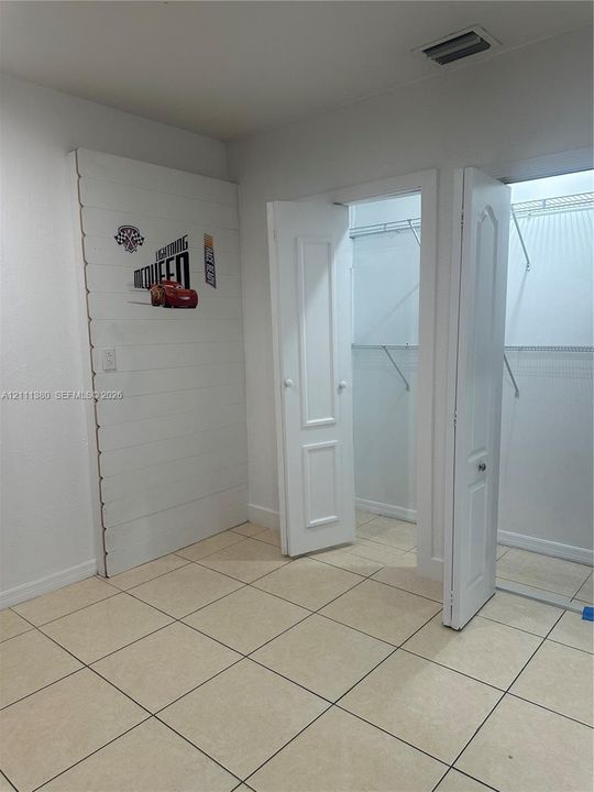 Neutral-toned ceramic tile flooring, white plank-style accent wall, and closet featuring dual paneled doors and wire shelving