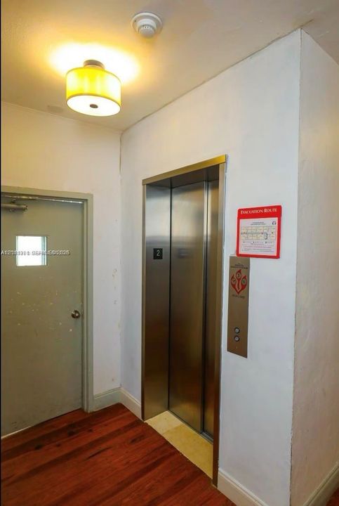 Elevator access with stainless steel doors, drum-style ceiling light fixture, and wood-finish flooring
