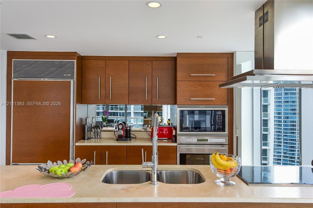 Kitchen featuring wood cabinetry with panel-ready integrated refrigerator, stone countertop, stainless steel dual-basin sink, and built-in stainless steel oven and microwave