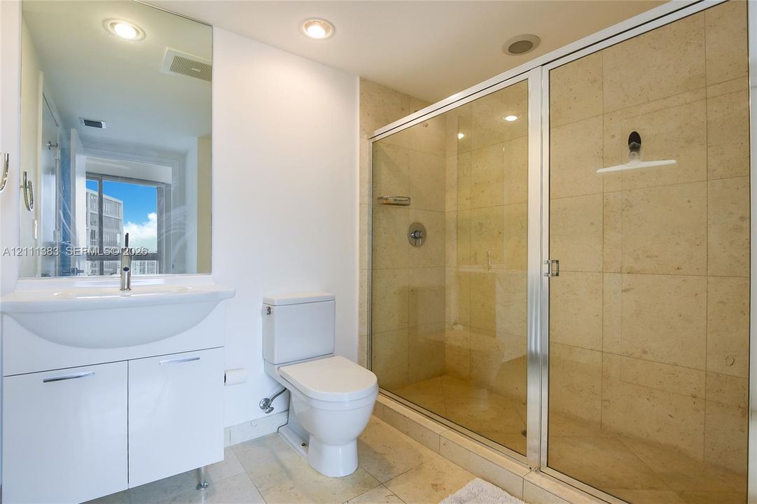 Bathroom featuring a walk-in shower with stone tile surround, glass enclosure, vanity with integrated sink, and large wall-mounted mirror