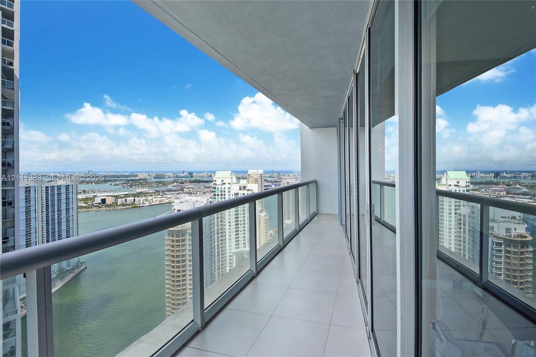 Covered balcony featuring tile flooring, full-height glass sliding doors, and a metal railing