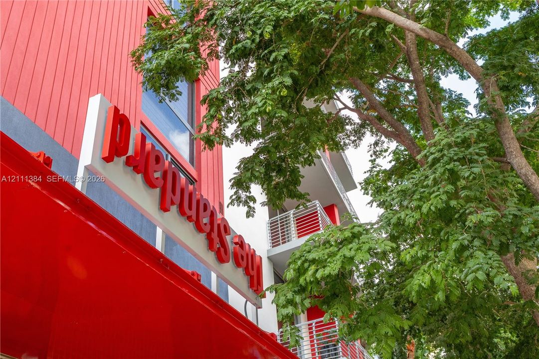 Vertical metal siding exterior with red accents, tiered balconies, and established trees