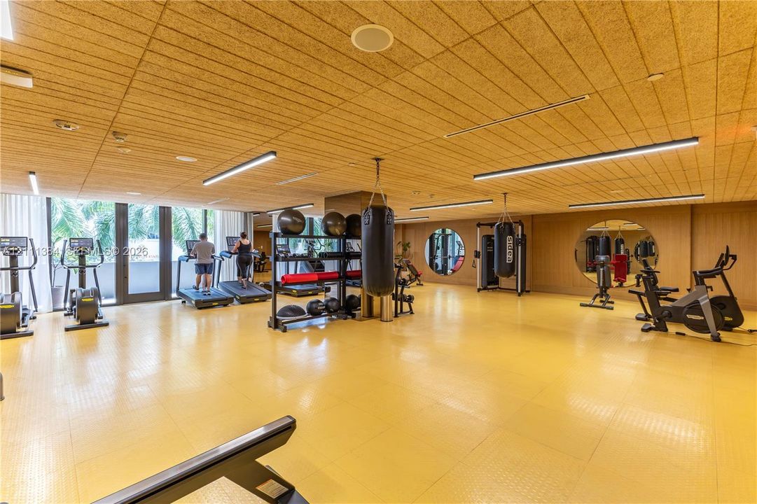 Fitness center featuring light-toned textured ceiling panels, recessed linear lighting, rubberized flooring, and circular wall mirrors