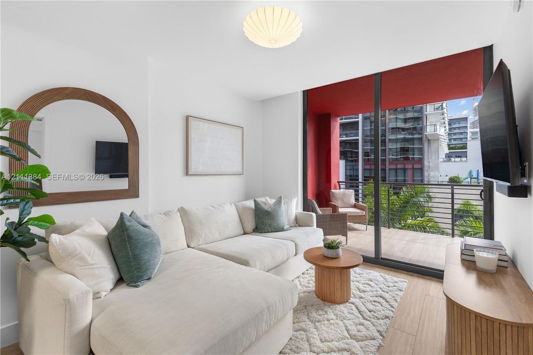Floor-to-ceiling sliding glass doors, private balcony with metal railing, wood-finish flooring, and recessed ceiling lighting