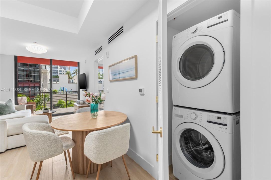 Stacked laundry unit in a dedicated closet, featuring floor-to-ceiling glass doors opening to an exterior balcony, tray ceiling, and wood-finish flooring