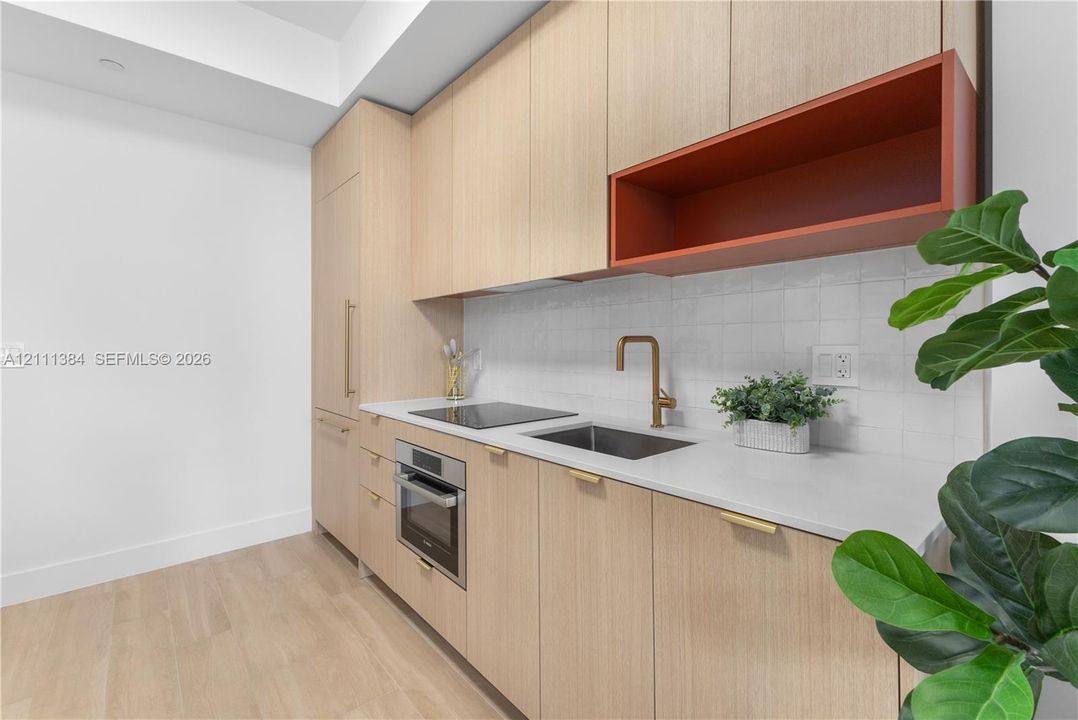Custom light wood-finish cabinetry, white tile backsplash, integrated appliances, light-toned countertop, and bronze-finish plumbing fixtures