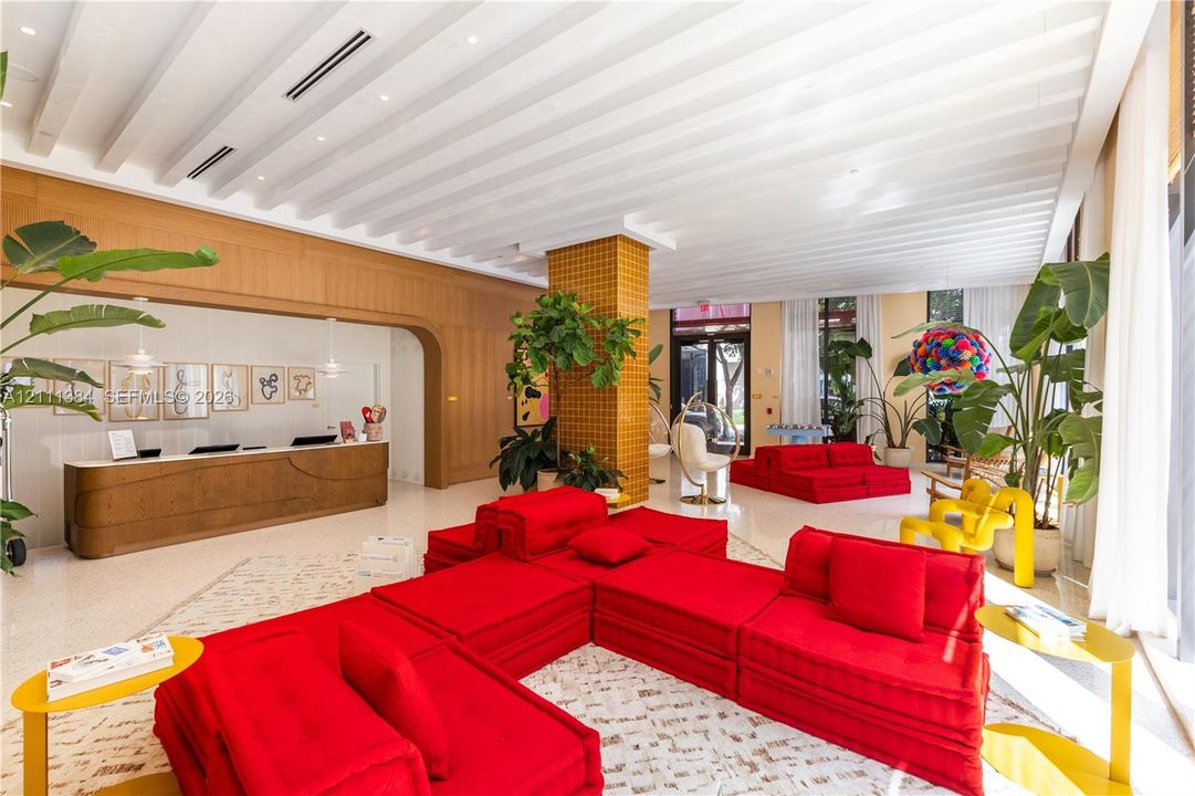 Expansive open-concept lobby featuring a coffered ceiling, custom wood-paneled wall, built-in reception desk, decorative tile-clad pillar, and light-toned terrazzo flooring