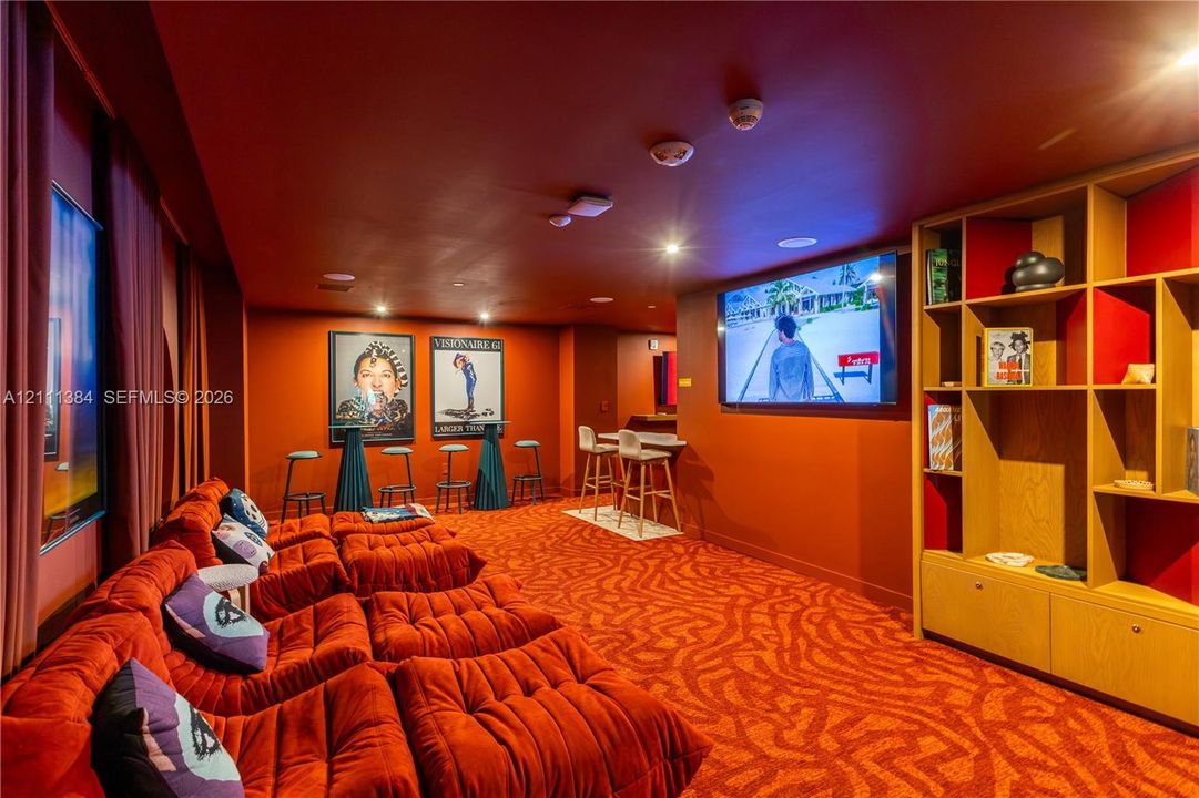 Dedicated screening room featuring a wall-mounted television, custom multi-tiered built-in shelving, recessed ceiling lighting, and patterned wall-to-wall carpeting