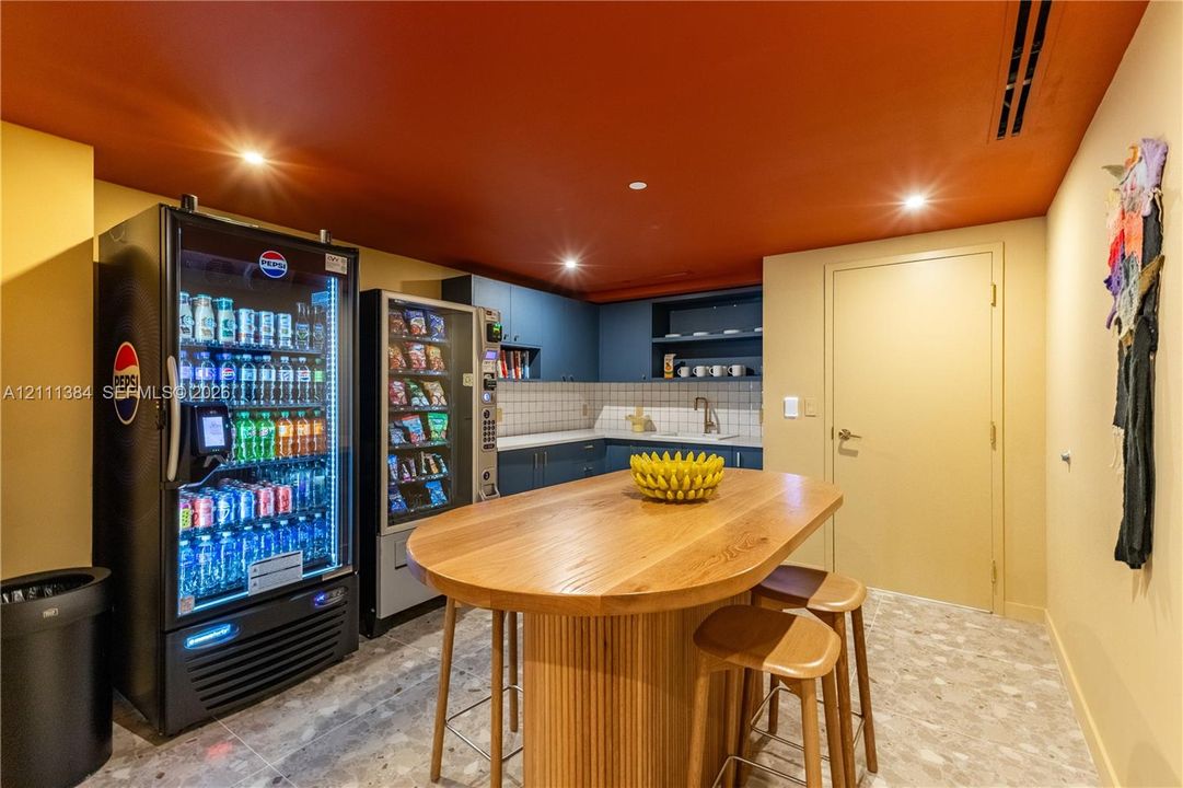 Kitchenette area featuring blue cabinetry, a square-tile backsplash, a recessed sink with a gooseneck faucet, and integrated refrigeration and vending units