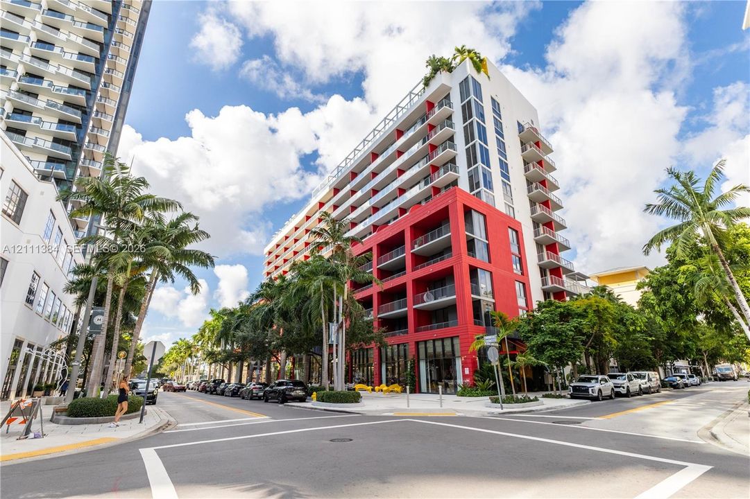 Multi-story high-rise exterior featuring a red and white facade, expansive glass windows, and private balconies with metal railings