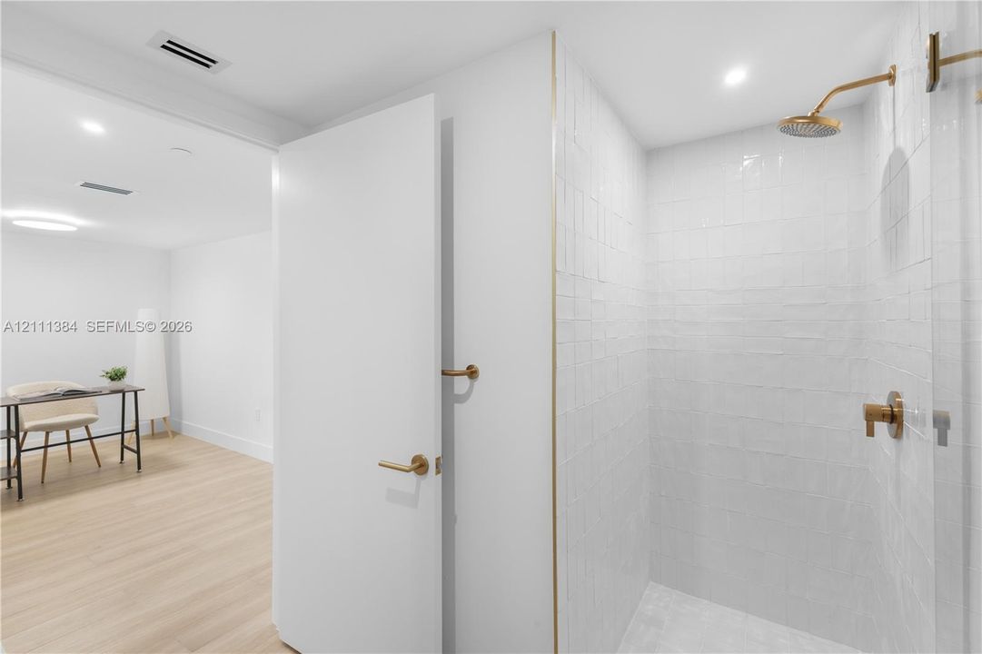 Walk-in shower with white gloss subway tile, gold-tone hardware, and glass enclosure, featuring wood-finish flooring and recessed lighting