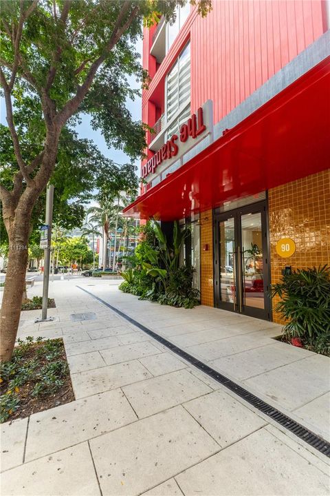Building exterior featuring a vibrant red facade, metallic awning, yellow tile accents, and glass-paned double entry doors