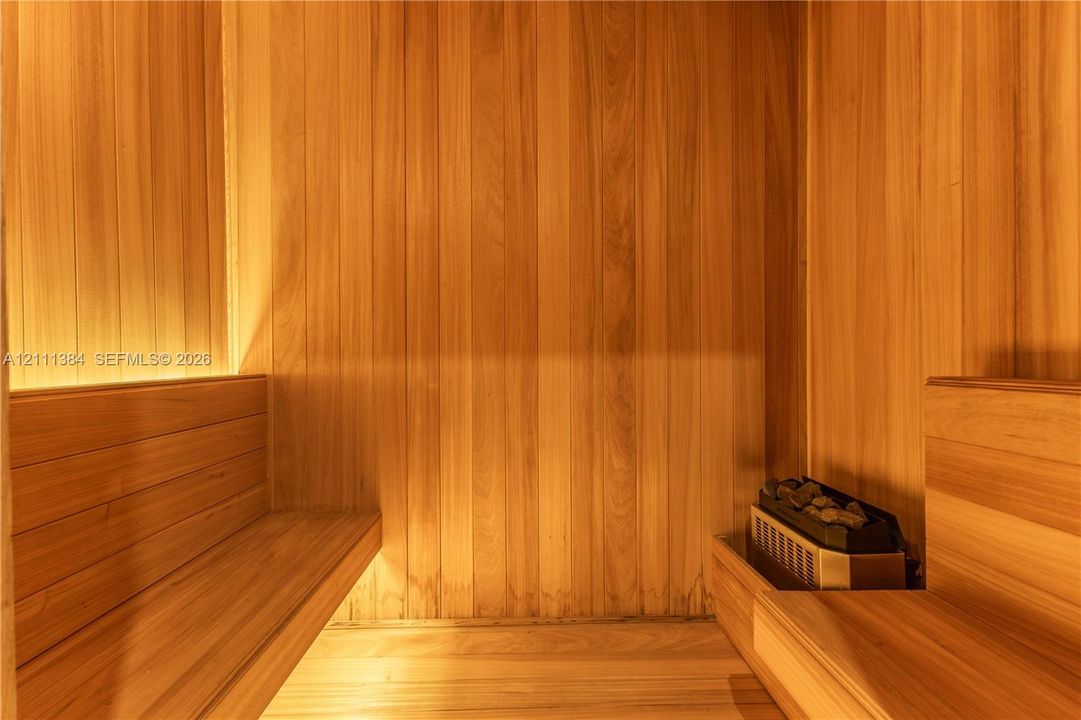 Custom sauna featuring vertical tongue-and-groove wood paneling, multi-level built-in bench seating, and an integrated heating element with stone accents