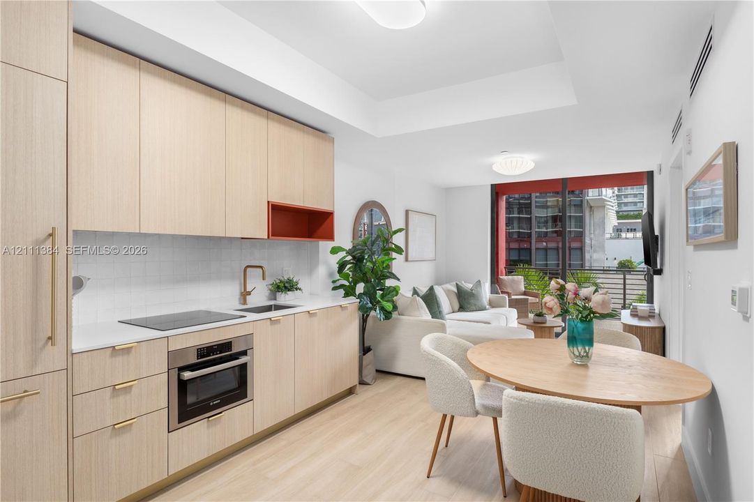 Kitchen featuring light wood-finish cabinetry, white solid-surface countertops, square tile backsplash, built-in stainless steel oven, and brass-tone fixtures