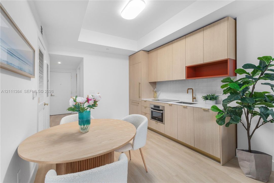Kitchen featuring light-tone wood cabinetry, built-in cooktop and oven, subway tile backsplash, matte finish hardware, and wood-finish flooring